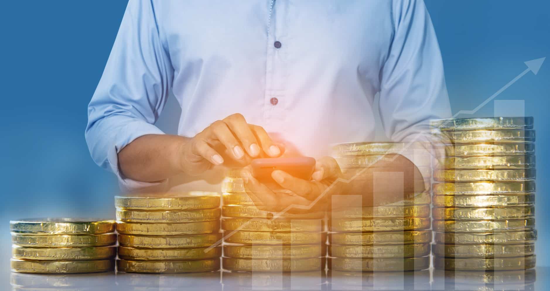 چند سکه طلا به صورت پله‌ای با یک نفر در بکگراند در حال کار کردن با گوشی خود